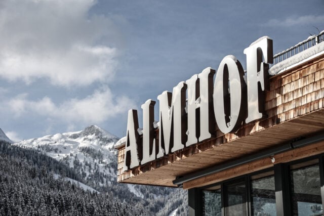 Almhof-Schild vor einer bergigen Winterlandschaft