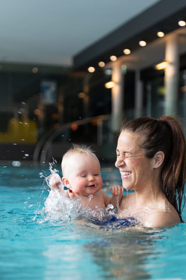 Mutter spielt mit Baby im Wasser.