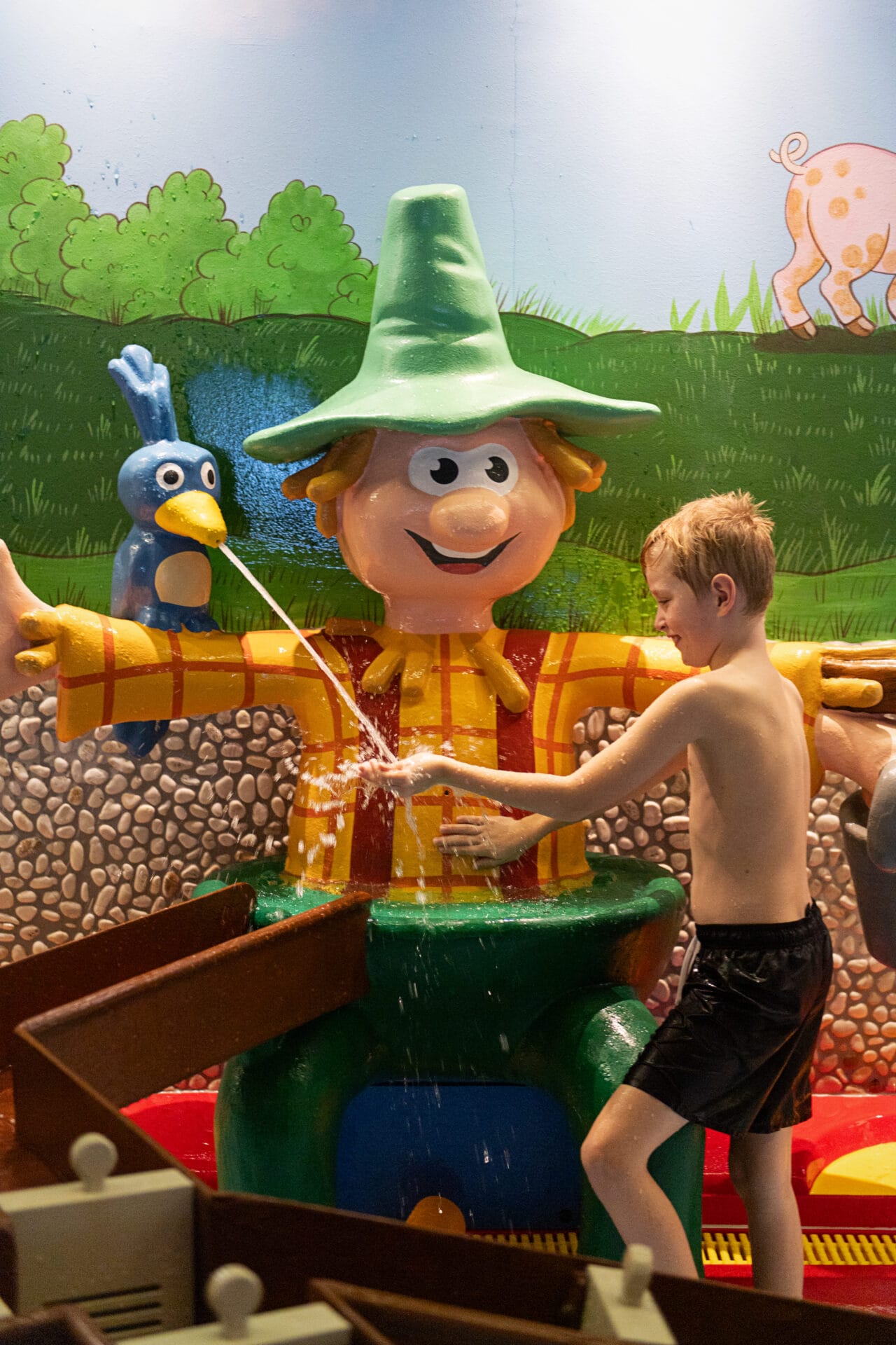 Kind spielt mit Wasser und Figuren im Hintergrund.